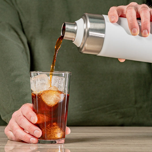 Cold Brew wird aus einer Thermoskanne in ein Glas mit Eiswürfeln gegossen