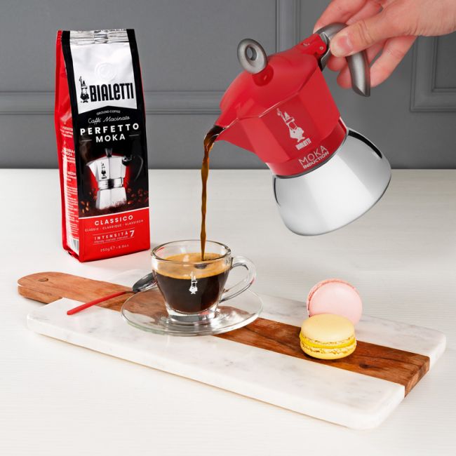 Bialetti Espressokocher in rot beim Einschenken eines Espressos in eine Tasse