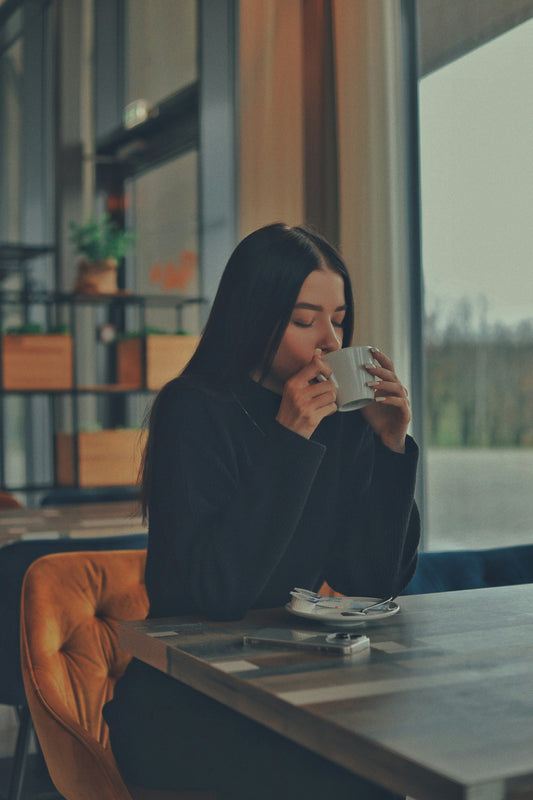Junge Frau sitzt am Tisch und trinkt eine Tassee Kaffee