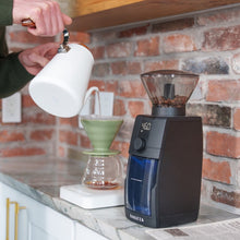 Load image into Gallery viewer, Baratza Encore ESP Pro elektrische Kaffeemühle schwarz, mit transprentem Bohnenbehälter, Seitenansicht der Mühle neben Pour-over Zubereitung