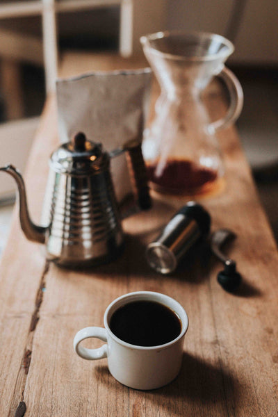 Tisch mit Kaffeetasse, Wasserkocher, Handmühle und Chemex Kaffeekaraffe